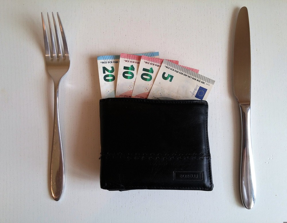 Das Bild zeigt Messer und Gabel. Dazwischen liegt statt einem Teller eine Geldbörse.